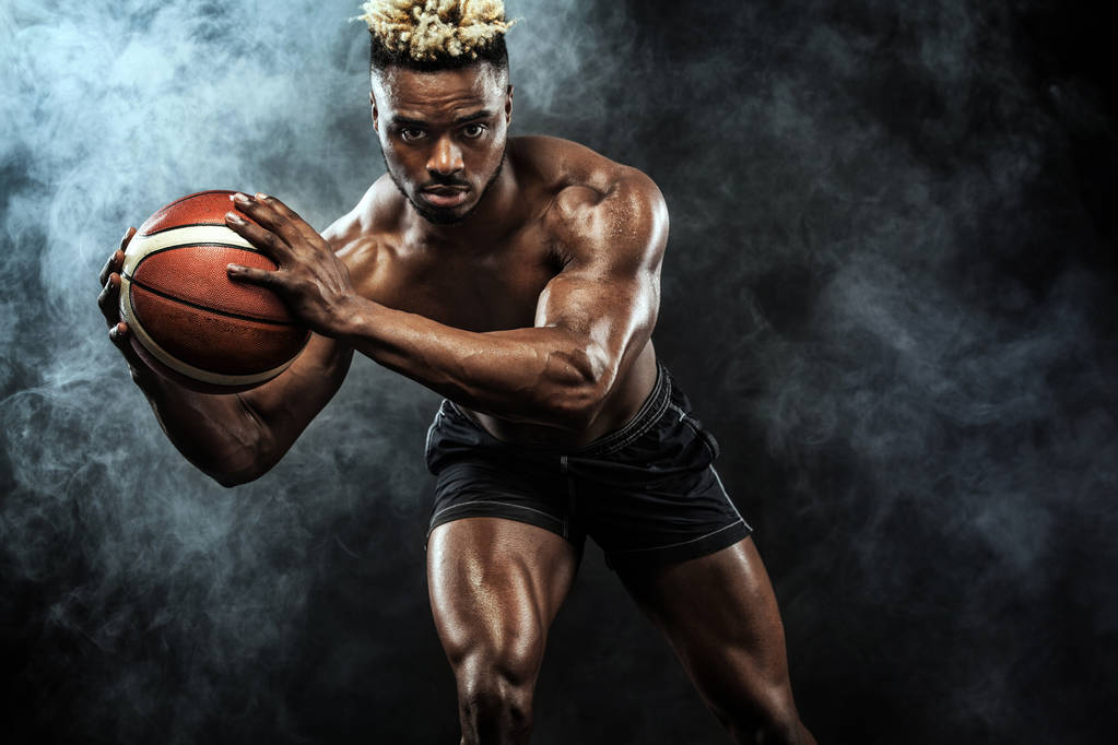 Retrato de deportista afroamericano, jugador de baloncesto con una pelota sobre fondo negro. Ajuste joven en ropa deportiva celebración de la pelota
. - Foto, Imagen