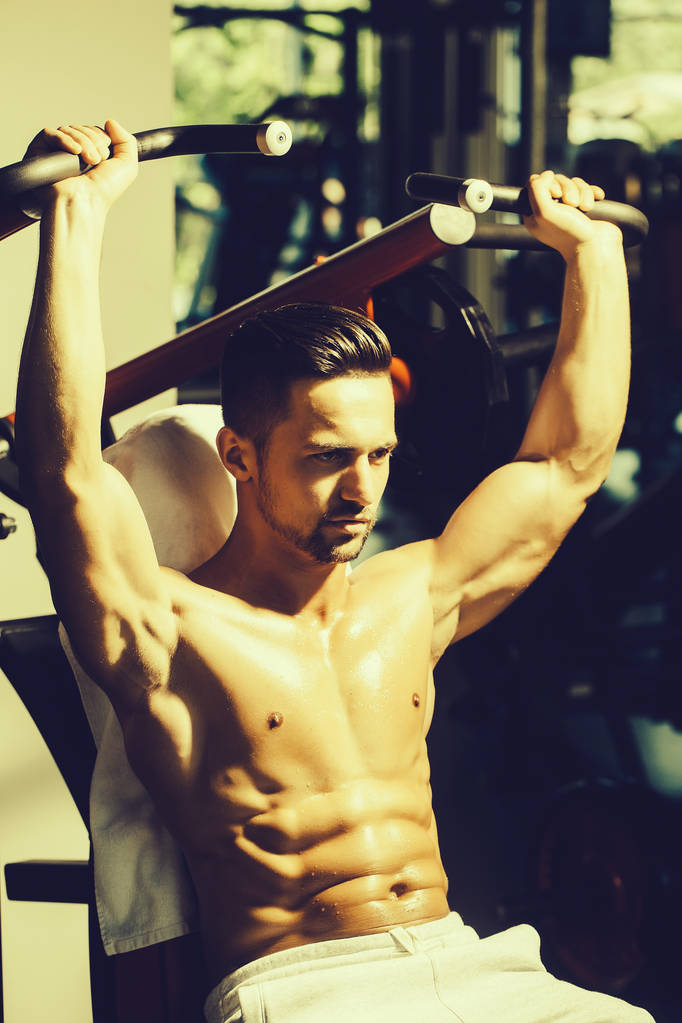 Hombre joven guapo con cuerpo húmedo muscular sexy y entrenamiento de espalda desnuda con equipo de ejercicio pesado en el gimnasio - Foto, imagen
