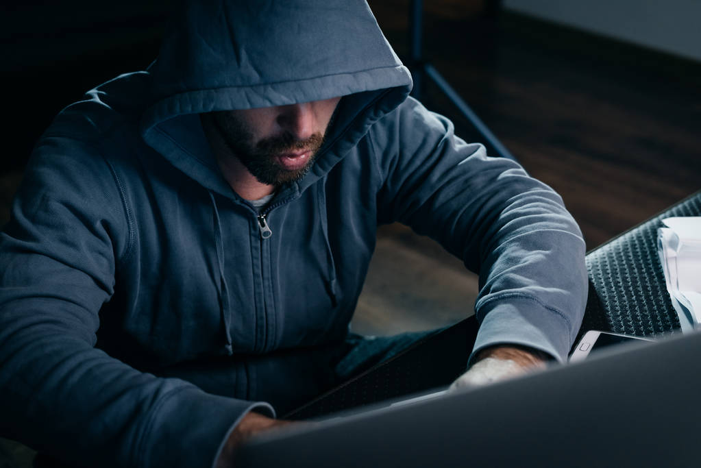 αρσενικό χάκερ στο κοστούμι με κουκούλα που κάθεται στο laptop - Φωτογραφία, εικόνα