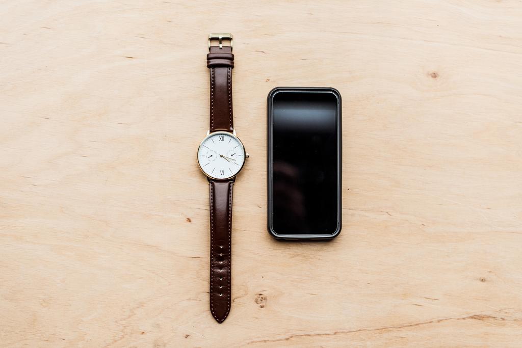 вид сверху на часы и выключенный смартфон на деревянном столе
 - Фото, изображение