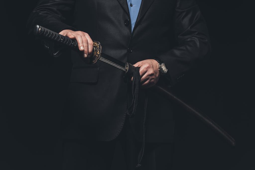 обрізаний знімок чоловіка в костюмі, що виймає меч катани ізольований на чорному
 - Фото, зображення