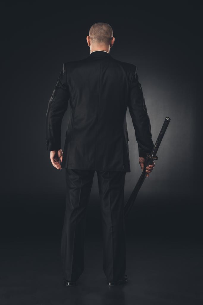 rear view of man in suit with katana sword on black - Photo, Image