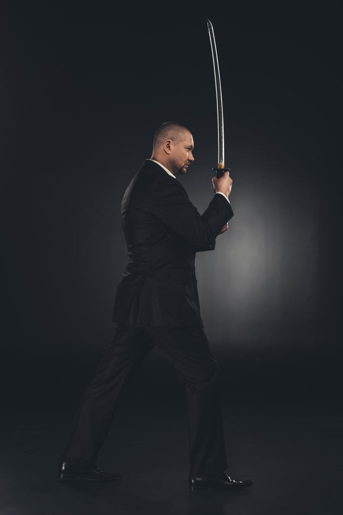 Seitenansicht eines Yakuza-Mitglieds im Anzug mit Katana-Schwert auf Schwarz - Foto, Bild
