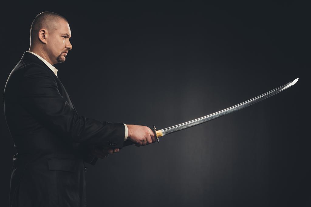 vue latérale de l'homme en costume avec épée katana isolé sur noir
 - Photo, image