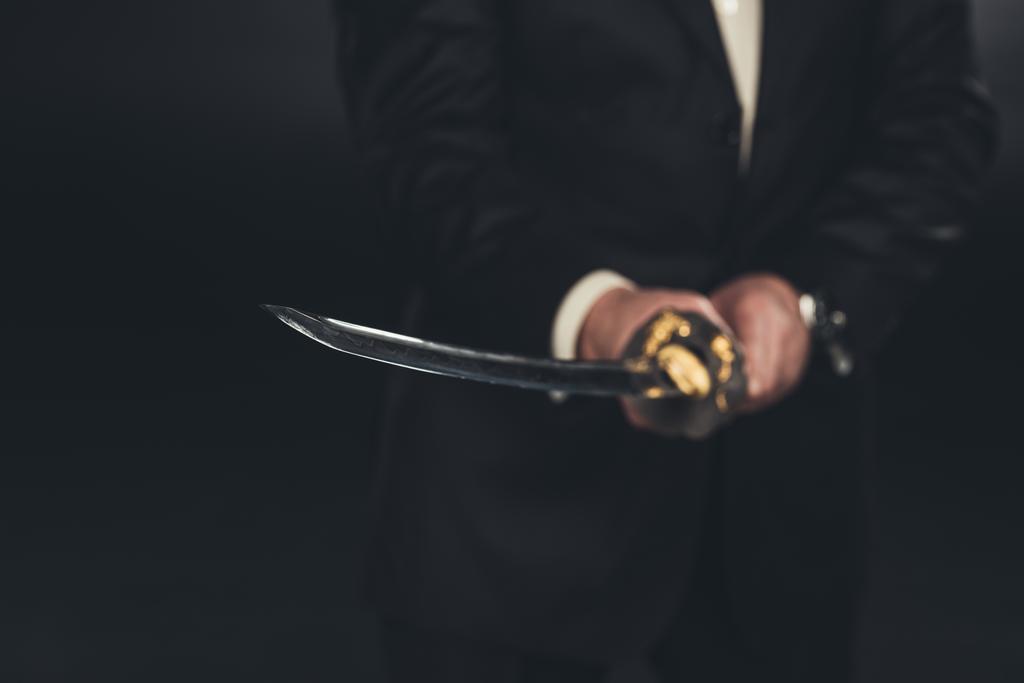 bijgesneden schot voor man in pak met katana zwaard op donkere achtergrond - Foto, afbeelding