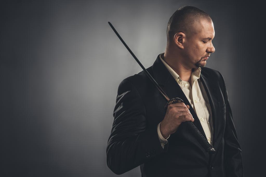 thoughtful man in suit with katana sword on black - Photo, Image