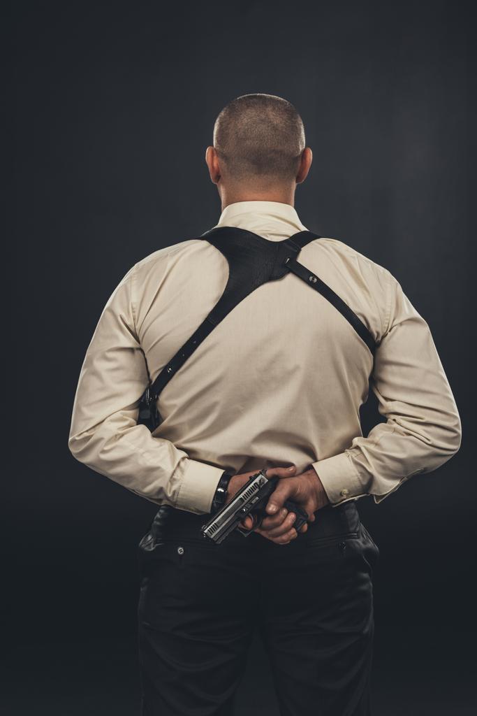 Achteraanzicht van de maffia lid in shirt houden pistool achter de rug - Foto, afbeelding