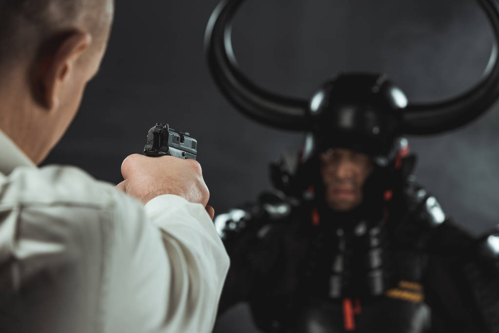Nahaufnahme eines Mannes, der mit einer Waffe auf gepanzerte Samurai zielt - Foto, Bild