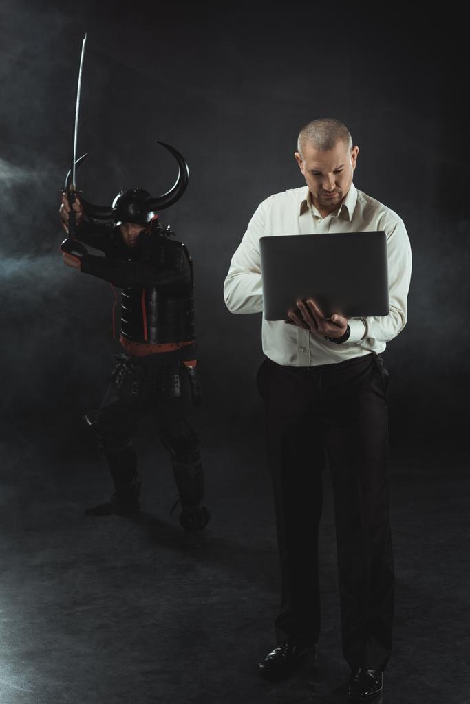 サムライの剣で彼の後ろに立っている間ノート パソコンを使用して集中している男 - 写真・画像
