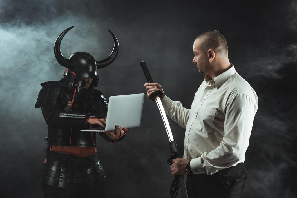 Mann mit Katana steht vor Samurai, während er Laptop benutzt - Foto, Bild