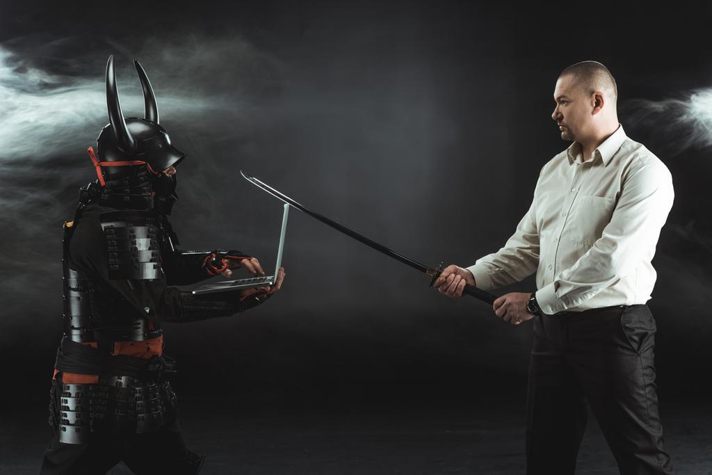 vista lateral del hombre con katana de pie en frente de samurai, mientras que el uso de la computadora portátil
 - Foto, Imagen
