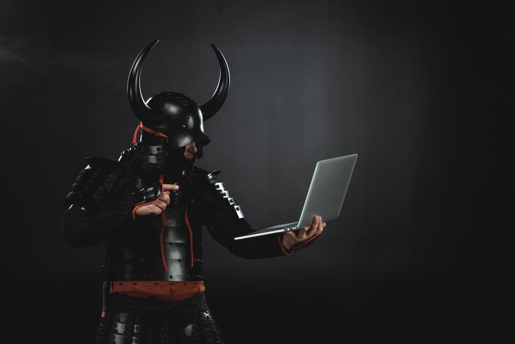 side view of armored samurai using laptop on black - Photo, Image