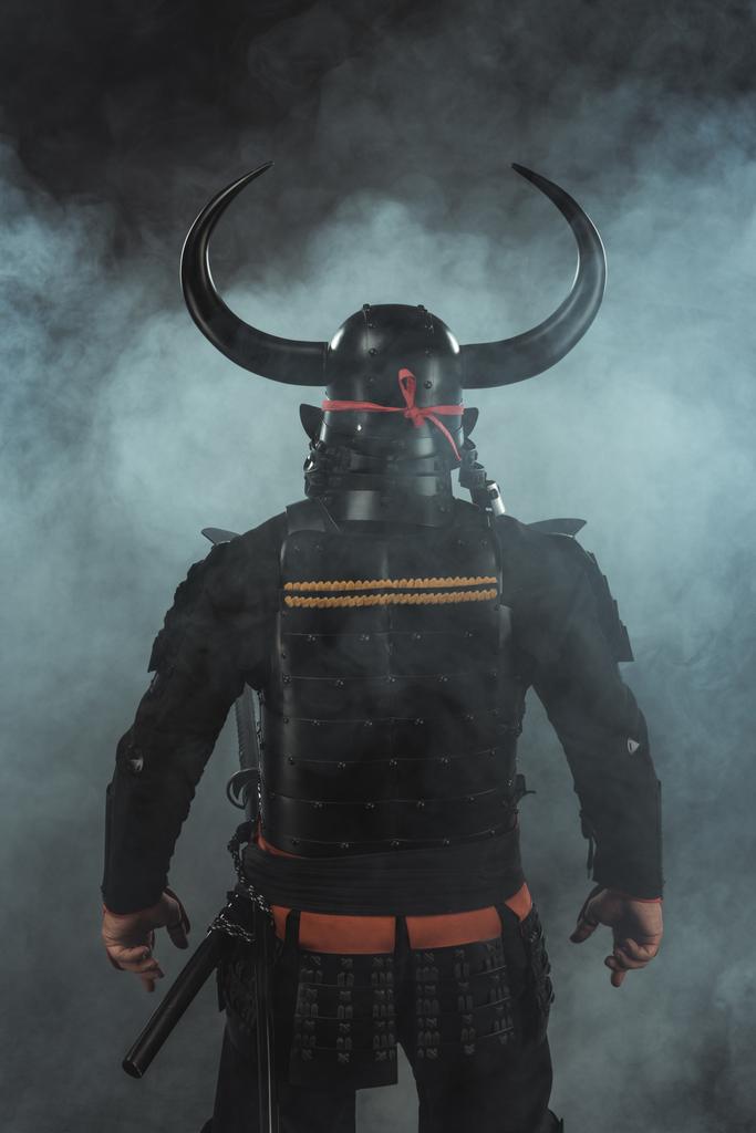 back view of samurai in traditional armor and horned helmet on dark background with smoke - Photo, Image