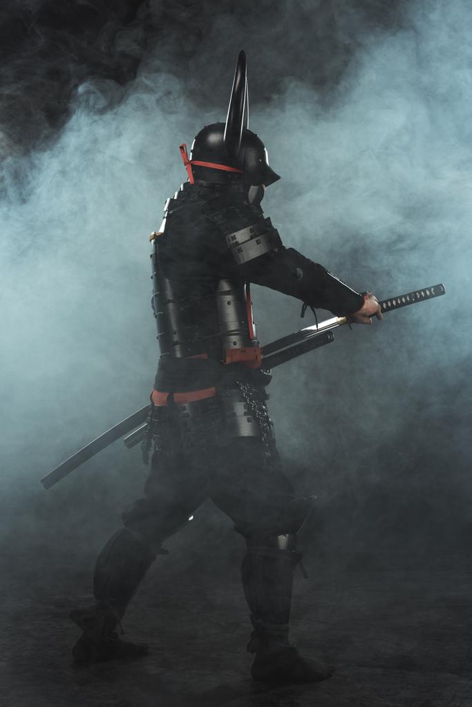 side view of samurai taking out his katana on dark background with smoke - Photo, Image