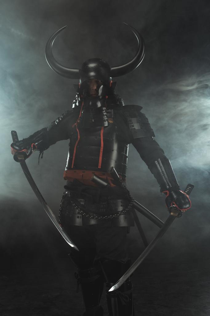 samuraj v tradiční zbroji s duální katana meče na tmavém pozadí s kouřem - Fotografie, Obrázek