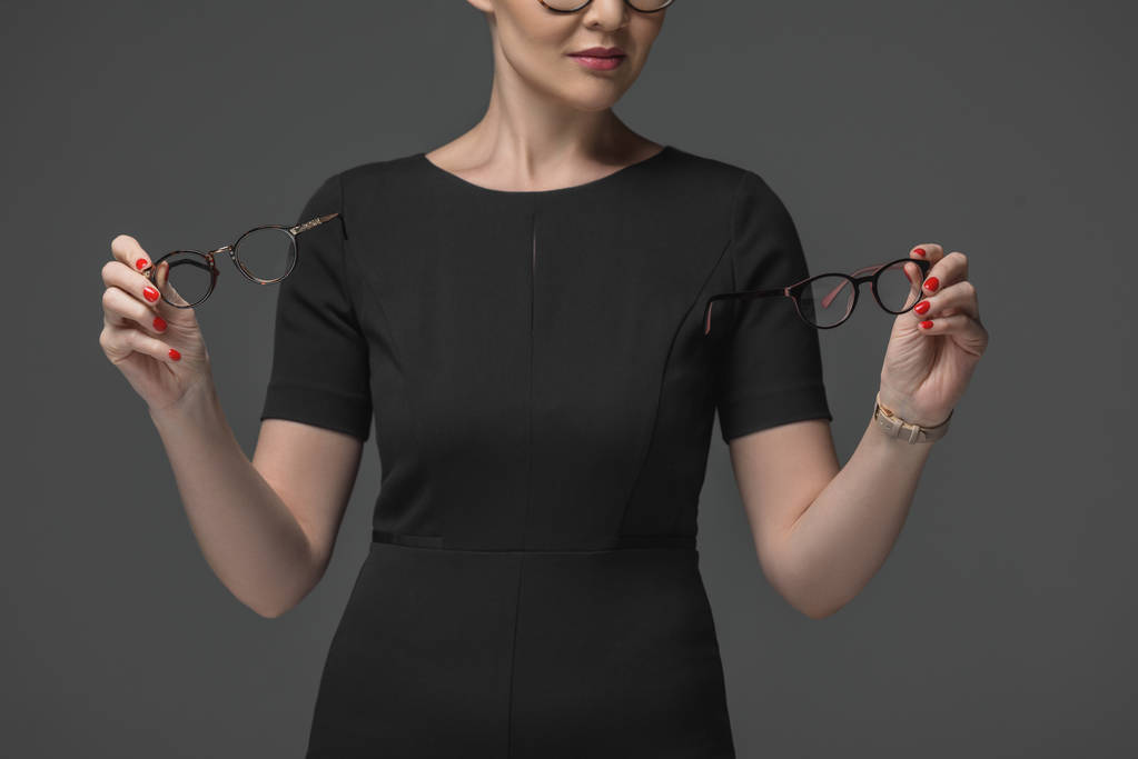 περικοπεί shot της γυναίκας σε μαύρο φόρεμα επιλέγοντας γυαλιά που απομονώνονται σε γκρι - Φωτογραφία, εικόνα