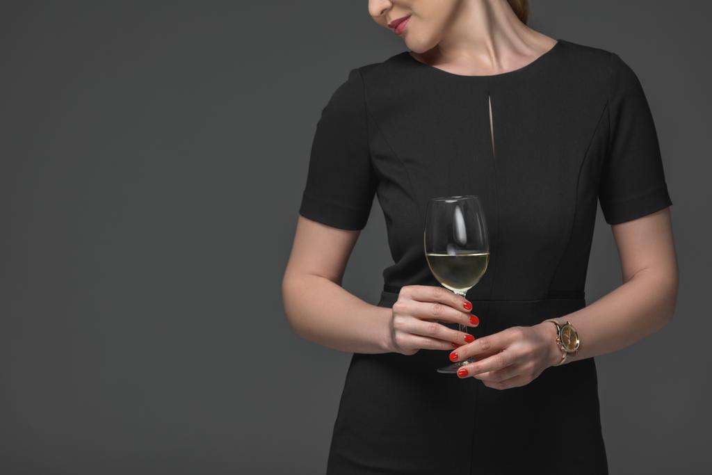 περικοπεί shot κομψή γυναίκα στο μαύρο φόρεμα που κρατά ποτήρι κρασί που απομονώνονται σε γκρι - Φωτογραφία, εικόνα