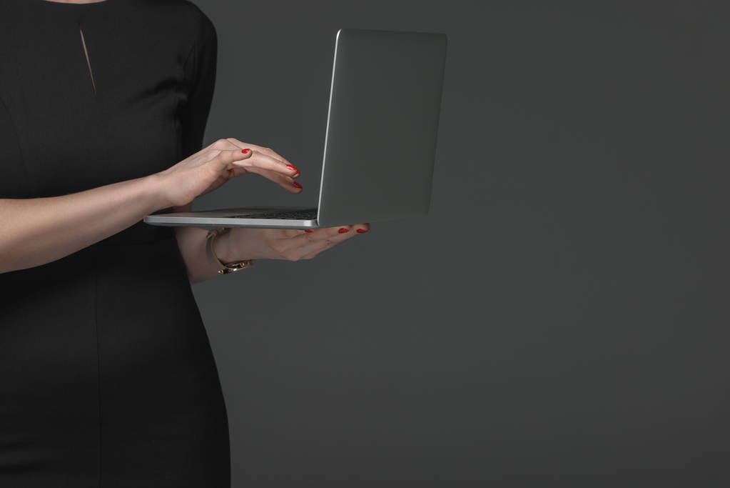 vue partielle rapprochée de la femme en robe noire à l'aide d'un ordinateur portable isolé sur gris
  - Photo, image