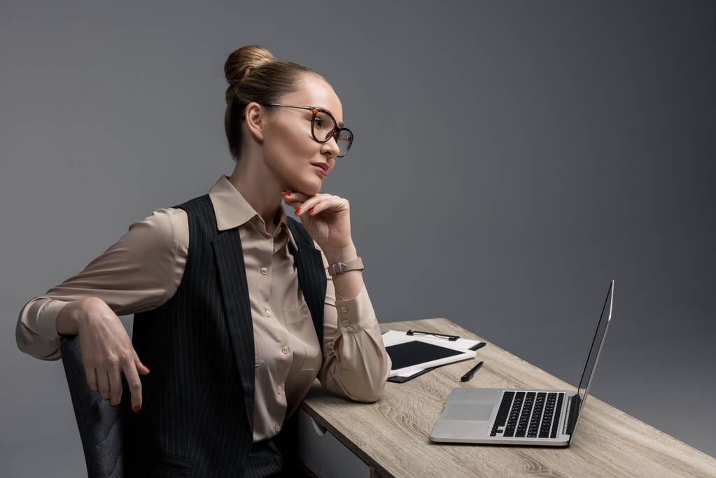 pensoso kazakh donna d'affari in occhiali da vista utilizzando computer portatile isolato su grigio
 - Foto, immagini