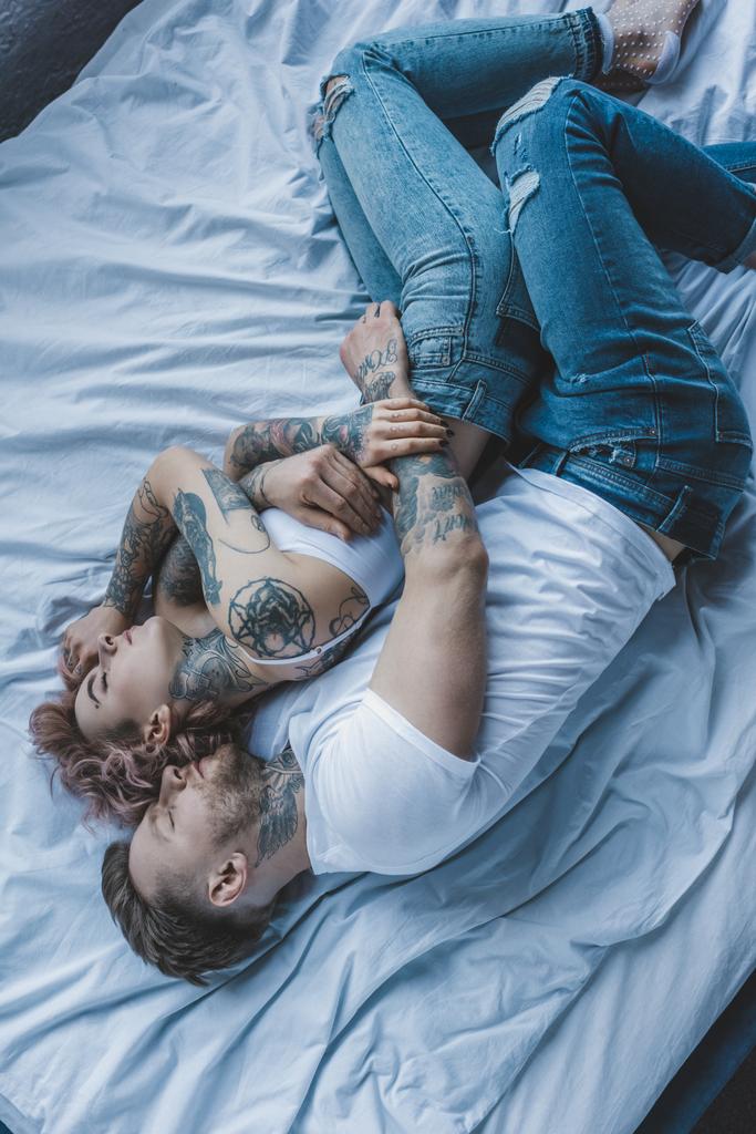top view of tattooed couple hugging and sleeping on bed - Photo, Image
