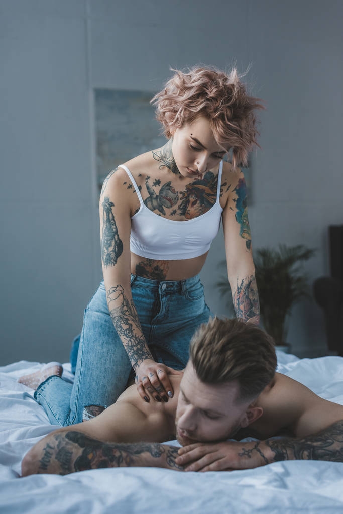 красива татуйована дівчина робить масаж для свого хлопця в ліжку
 - Фото, зображення
