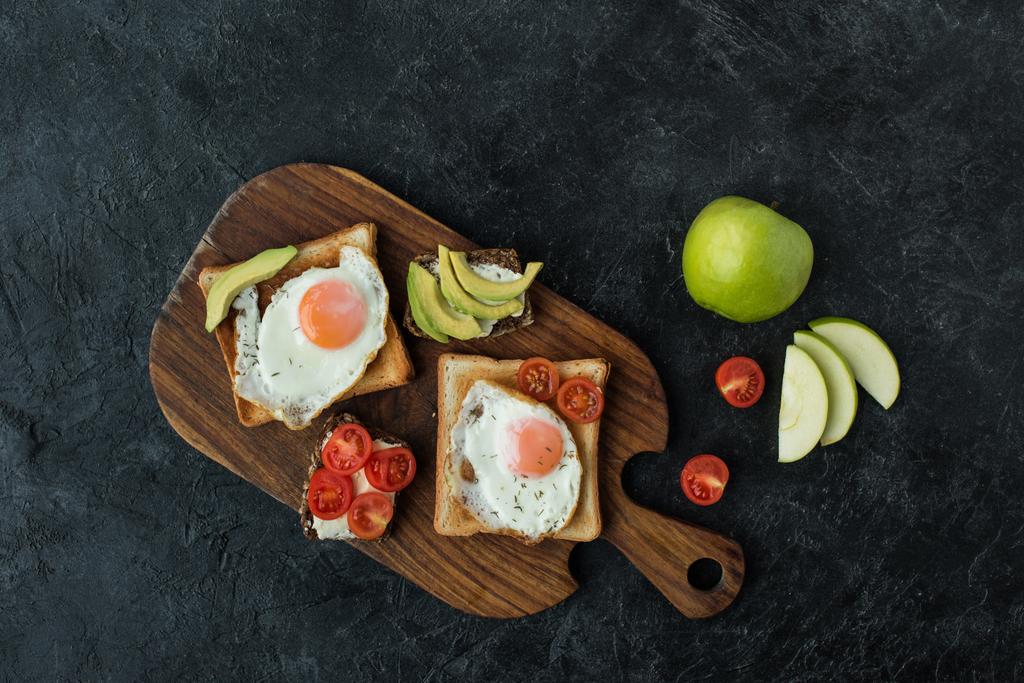 вид зверху на тости зі смаженими яйцями на сніданок на дерев'яній обробній дошці на темній поверхні
 - Фото, зображення