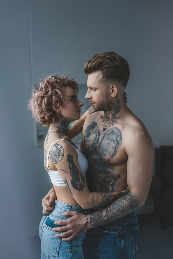 nuori tatuoitu pari syleilee makuuhuoneessa
 - Valokuva, kuva