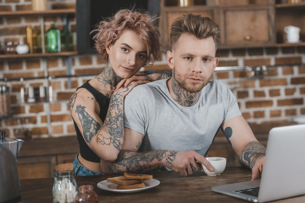 tattooed couple using laptop and eating breakfast in kitchen - Photo, Image