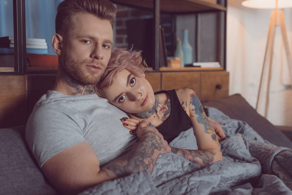 hermosa pareja tatuada relajándose en la cama en casa
 - Foto, imagen