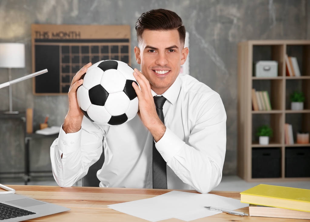 Гарний менеджер з футбольним м'ячем, що сидить на робочому місці
 - Фото, зображення