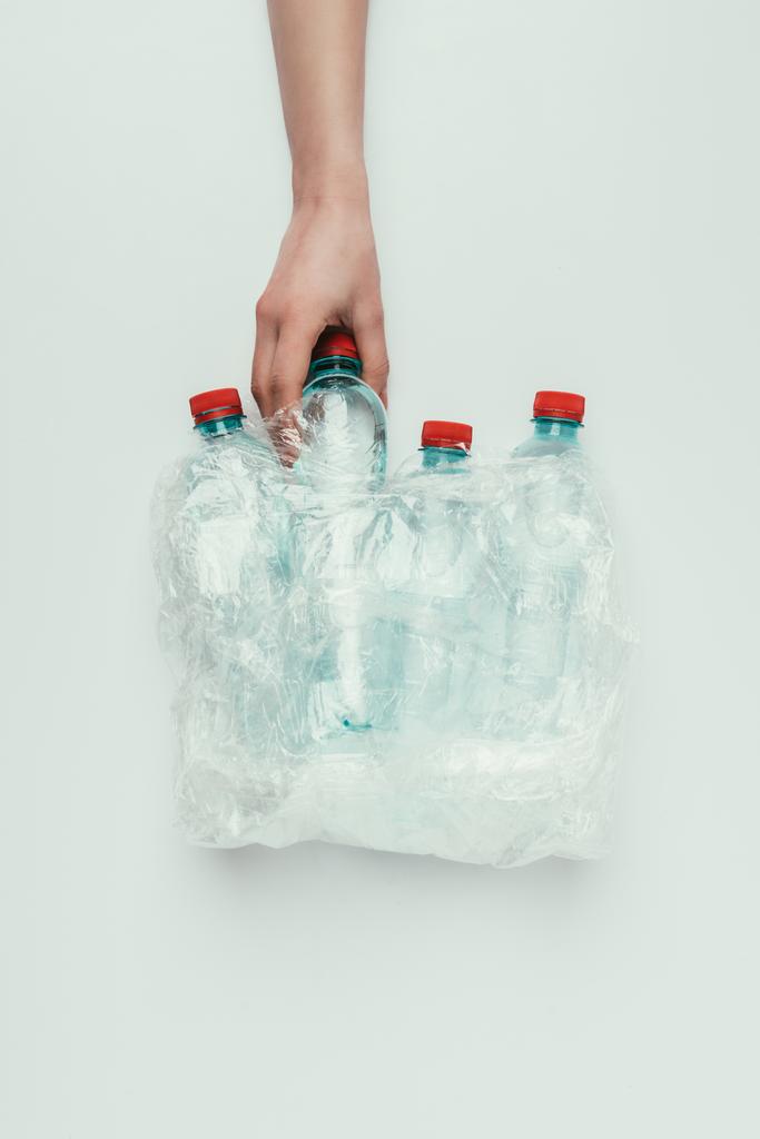 Μερική άποψη της γυναίκας λαμβάνοντας πλαστικό μπουκάλι από πλαστική σακούλα που απομονώνονται σε γκρι - Φωτογραφία, εικόνα