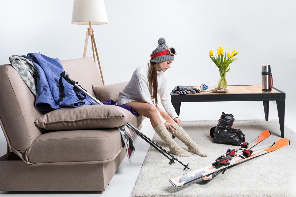 молодая спортсменка в теплых носках, на полу лежит лыжное снаряжение
 - Фото, изображение