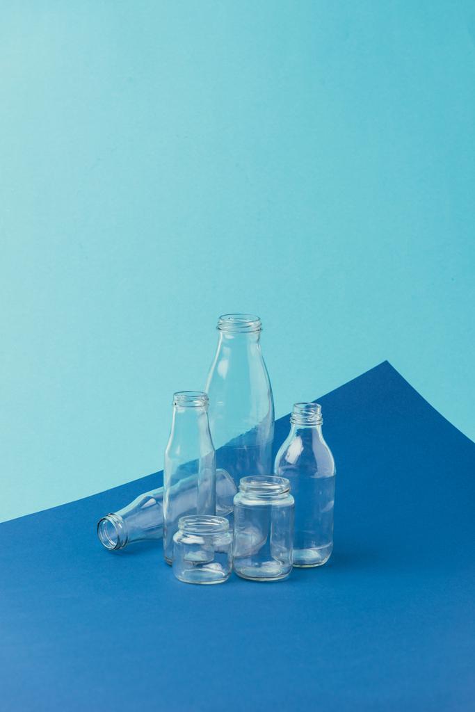 κλείνω πάνω θέα από διάφορα γυάλινα μπουκάλια και βάζα σε μπλε φόντο, η έννοια της ανακύκλωσης - Φωτογραφία, εικόνα