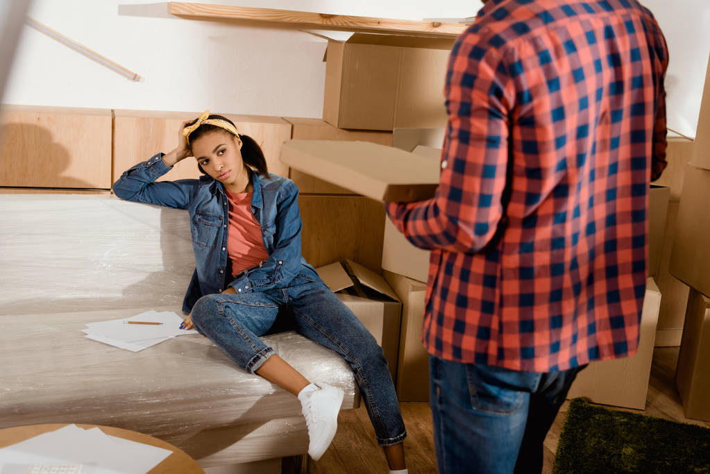 stanca ragazza afroamericana guardando il suo ragazzo con la pizza, trasferirsi in un nuovo appartamento
 - Foto, immagini