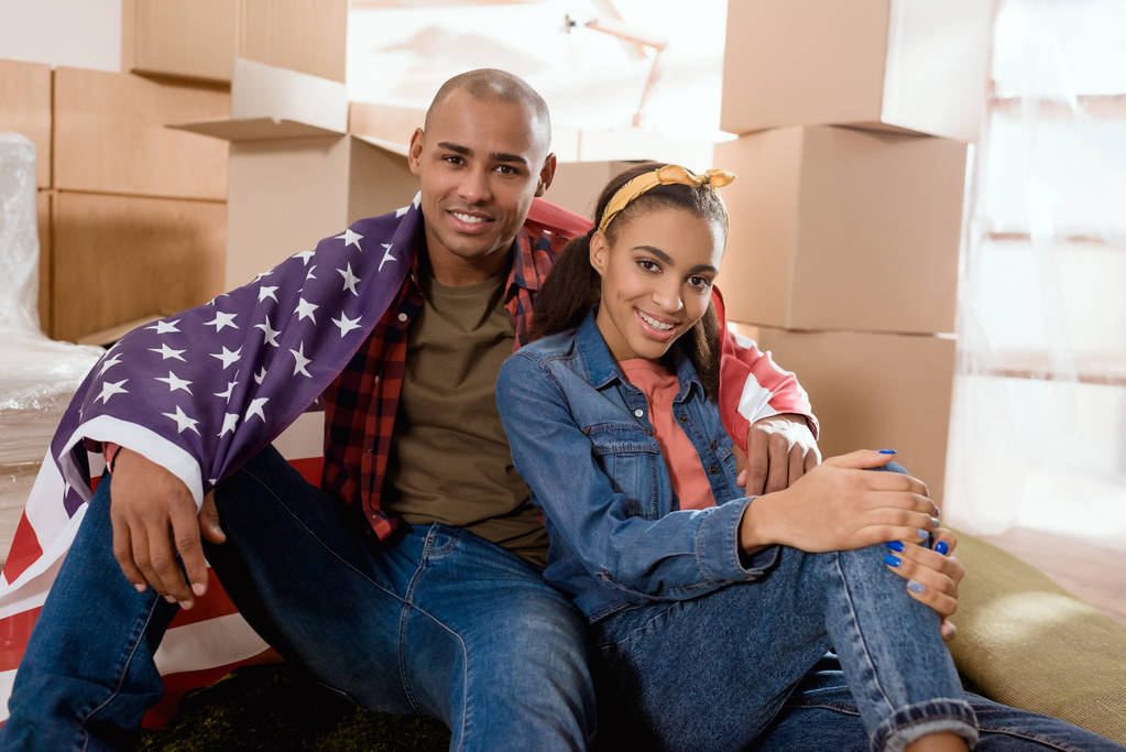 casal afro-americano com bandeira dos estados unidos sentado no chão em nova casa com caixas de papelão
 - Foto, Imagem