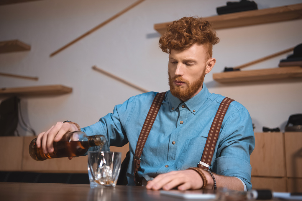 schöner stylischer junger Mann gießt Whisky aus Flasche in Glas - Foto, Bild