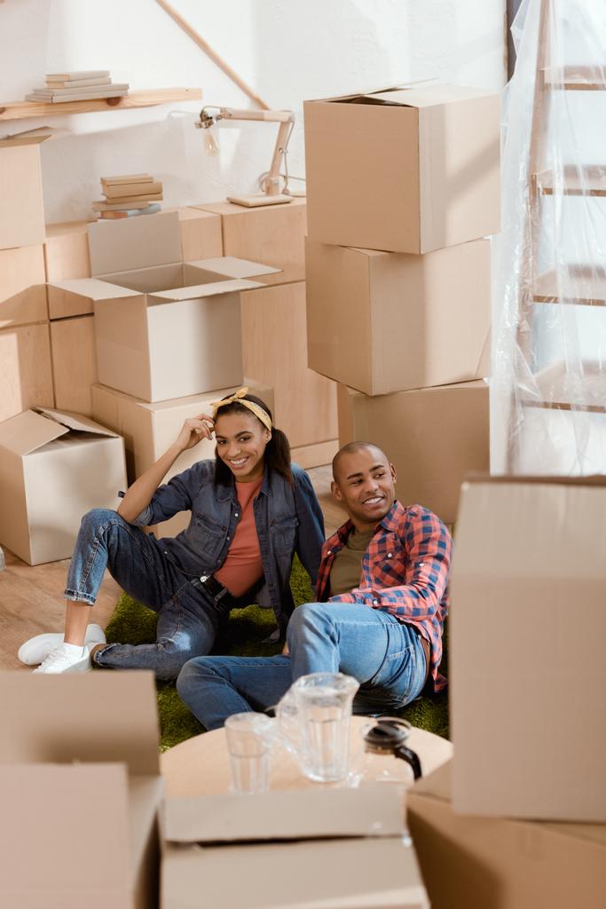 pareja afroamericana descansando en el suelo en un nuevo hogar con cajas de cartón
 - Foto, Imagen