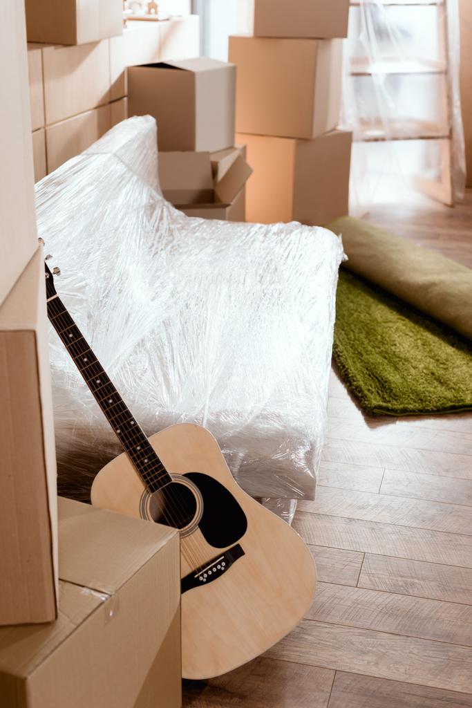 sofa, akoestische gitaar, vakken tapijt en karton gerold in nieuwe woning - Foto, afbeelding
