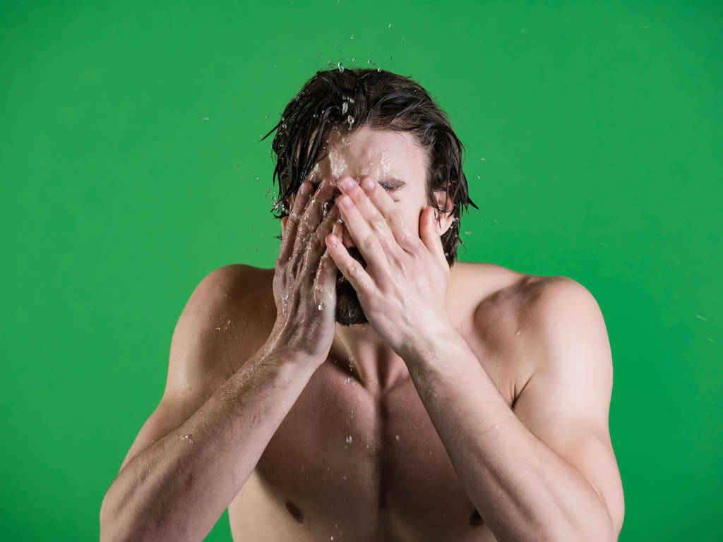Uomo spruzzi d'acqua a faccia su sfondo verde
. - Foto, immagini