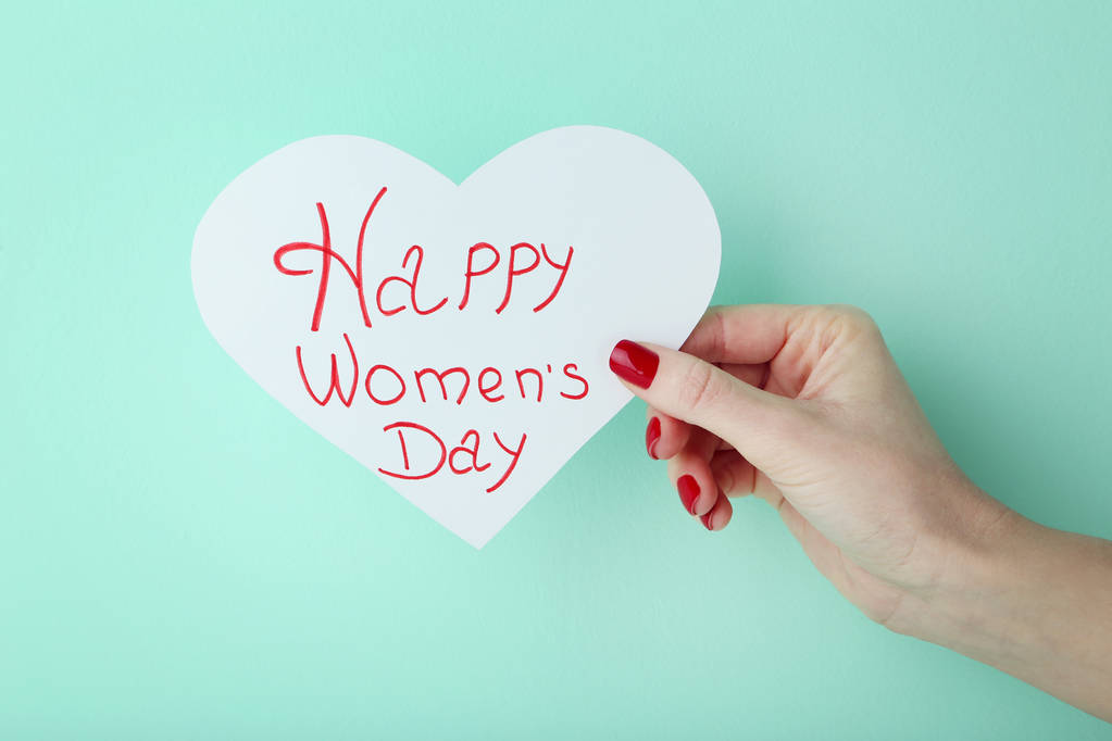 Vrouwelijke hand met kaart met inscriptie gelukkig Vrouwendag op mint achtergrond - Foto, afbeelding