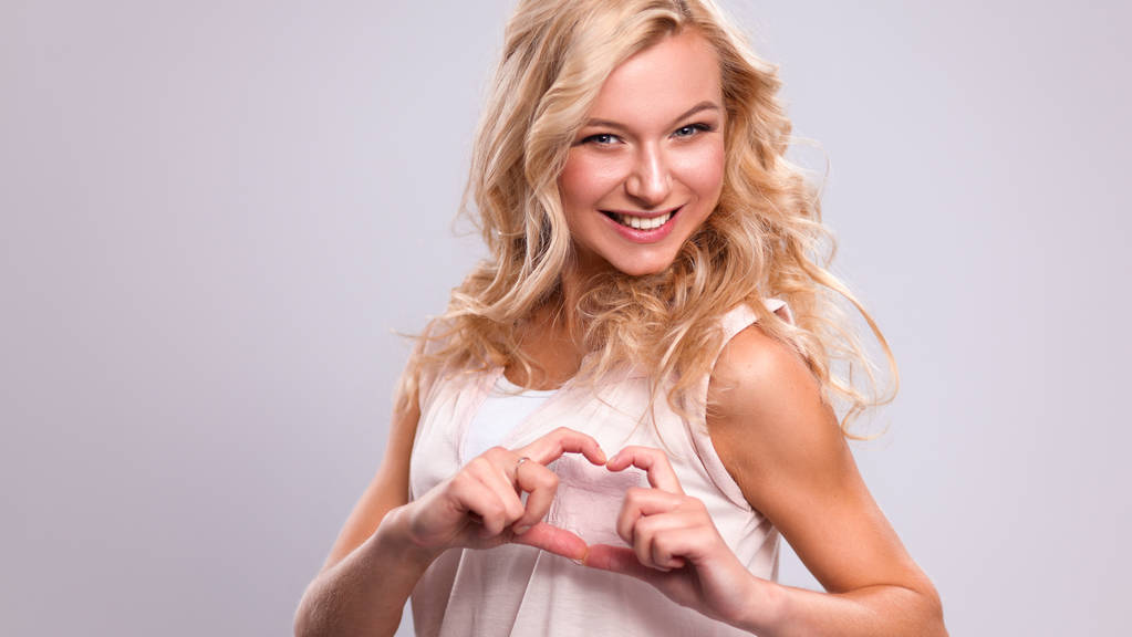 Lachende meisje in witte shirts tonen hart met handen - Foto, afbeelding