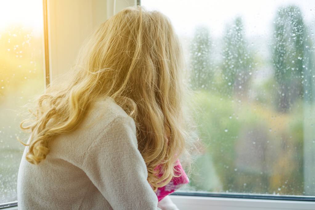 Uma criança de pijama sorri em uma janela de outono com gotas de chuva
. - Foto, Imagem