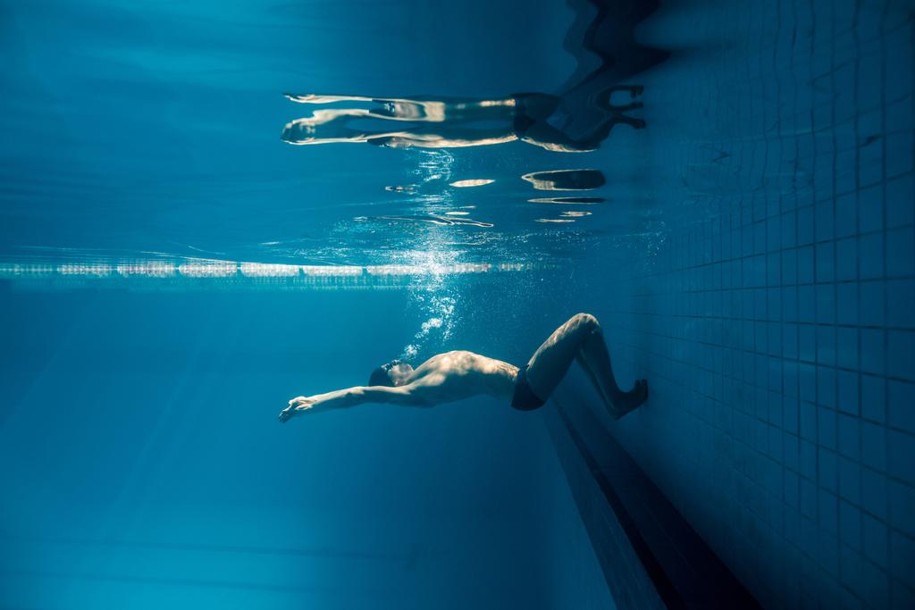 onderwater foto van jonge zwemmer in bril uitoefenen in zwembad - Foto, afbeelding
