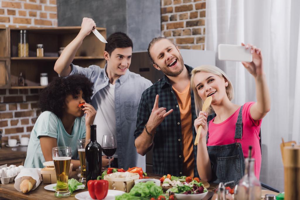 улыбающиеся мультикультурные друзья делают селфи со смартфоном на кухне
 - Фото, изображение