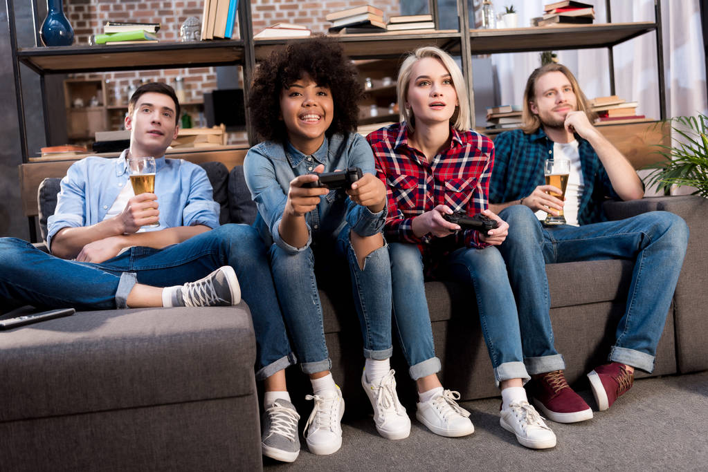 мультикультурні дівчата грають у відеоігри на дивані вдома, чоловіки п'ють пиво
 - Фото, зображення