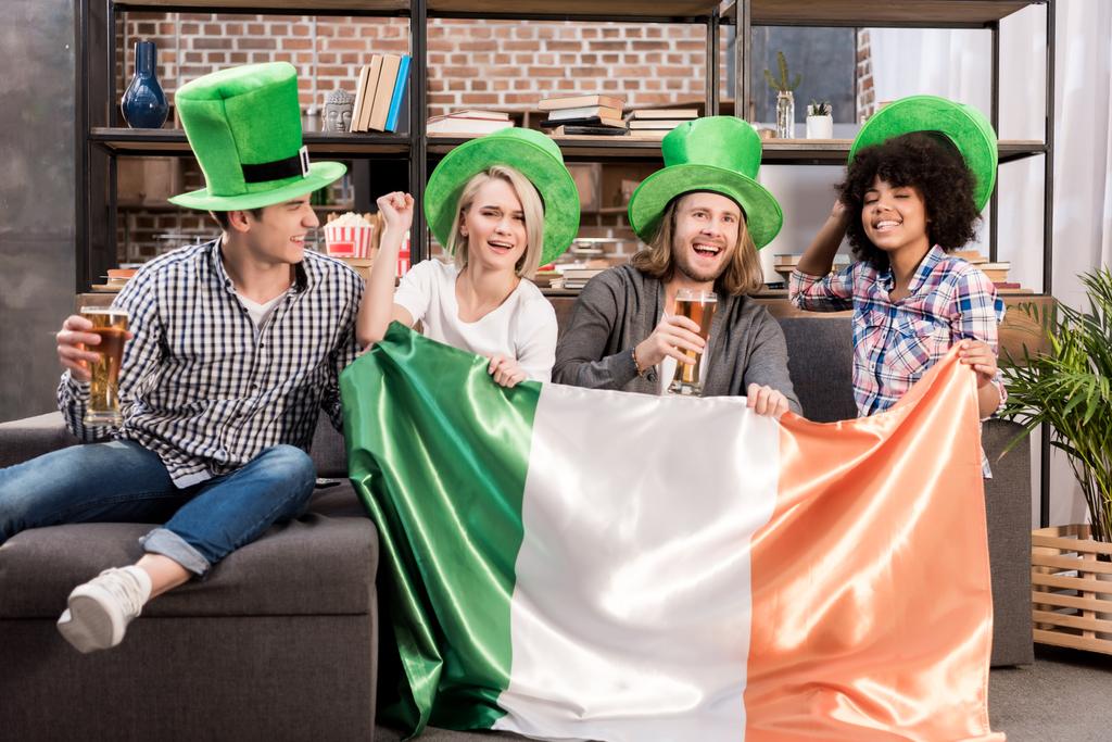 happy multicultural friends watching tv on saint patrick day with irish flag - Photo, Image
