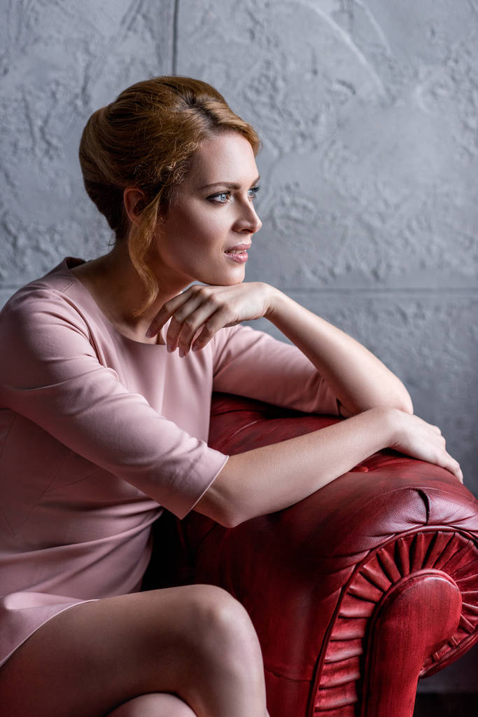 rózsaszín ruha karosszékben ül, és keres el-gondolkodó fiatal nő - Fotó, kép