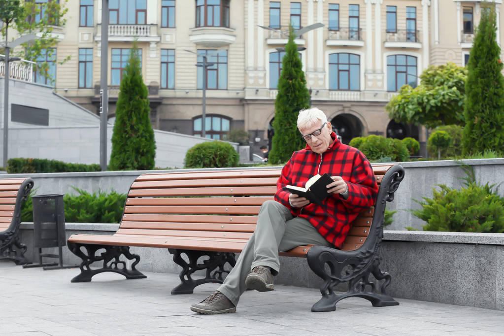 Όμορφος ώριμος άνδρας, διαβάζοντας το βιβλίο στον πάγκο σε εξωτερικούς χώρους - Φωτογραφία, εικόνα