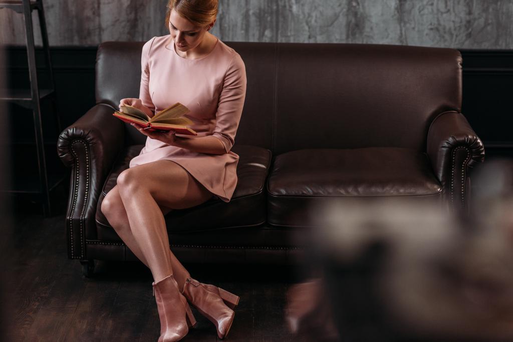 привлекательная молодая женщина читает книгу на диване в интерьере лофта
 - Фото, изображение
