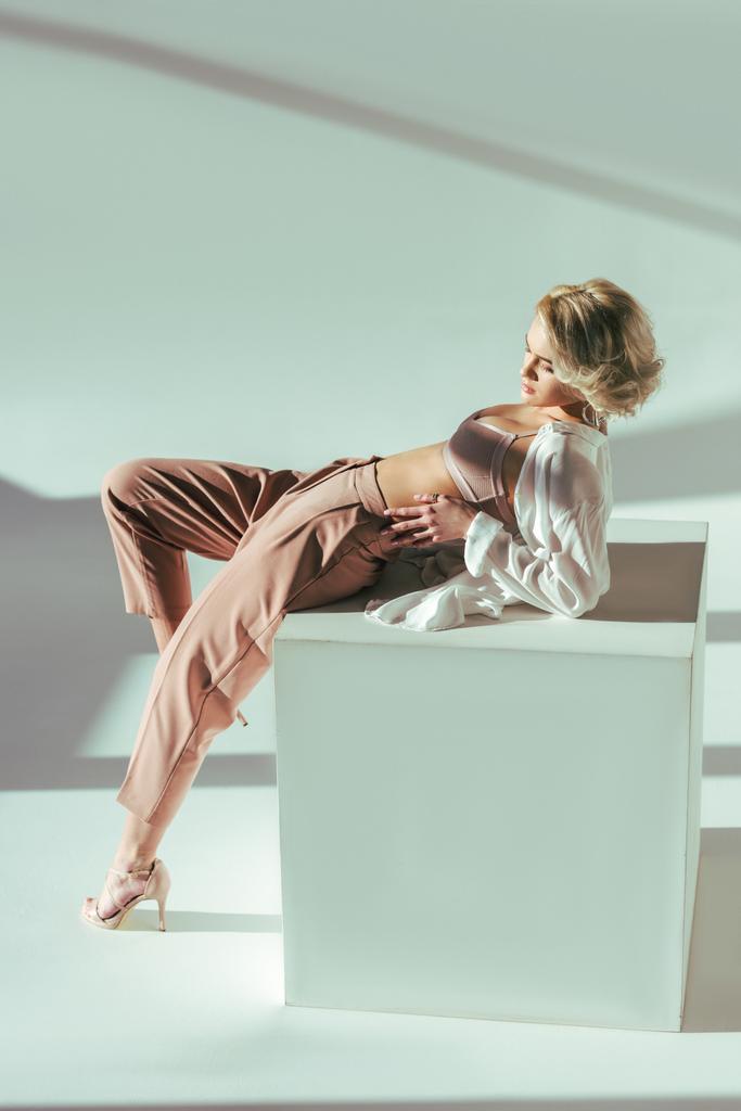 Вид в полный рост красивой стильной блондинки в розовом бюстгальтере, рубашке и брюках, лежащей в студии
   - Фото, изображение